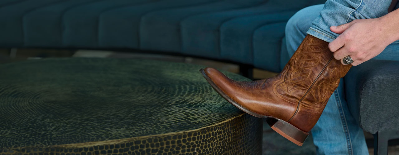 A man with his foot on a table putting on a pair of Tony Lama boots.